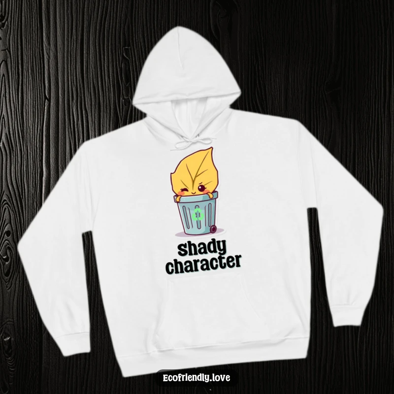 Funny hoodie with a mischievous leaf character winking from behind a small recycling bin, cozy and clever.
